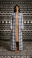 Woman wearing a long blue and white checkered coat against a patterned wall.
