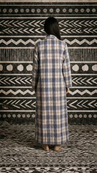 Person wearing a long, plaid coat standing in front of a patterned wall.
