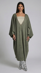 Woman wearing a long olive green dress with a plain background