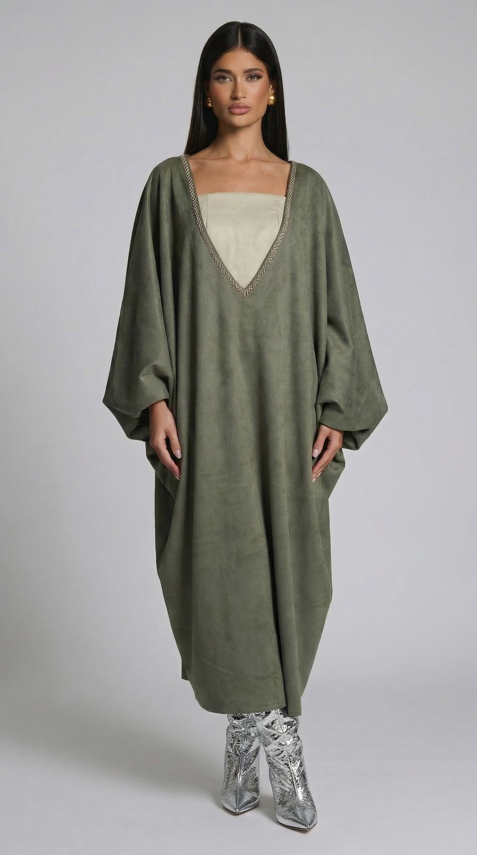 Woman wearing a long olive green dress with a plain background