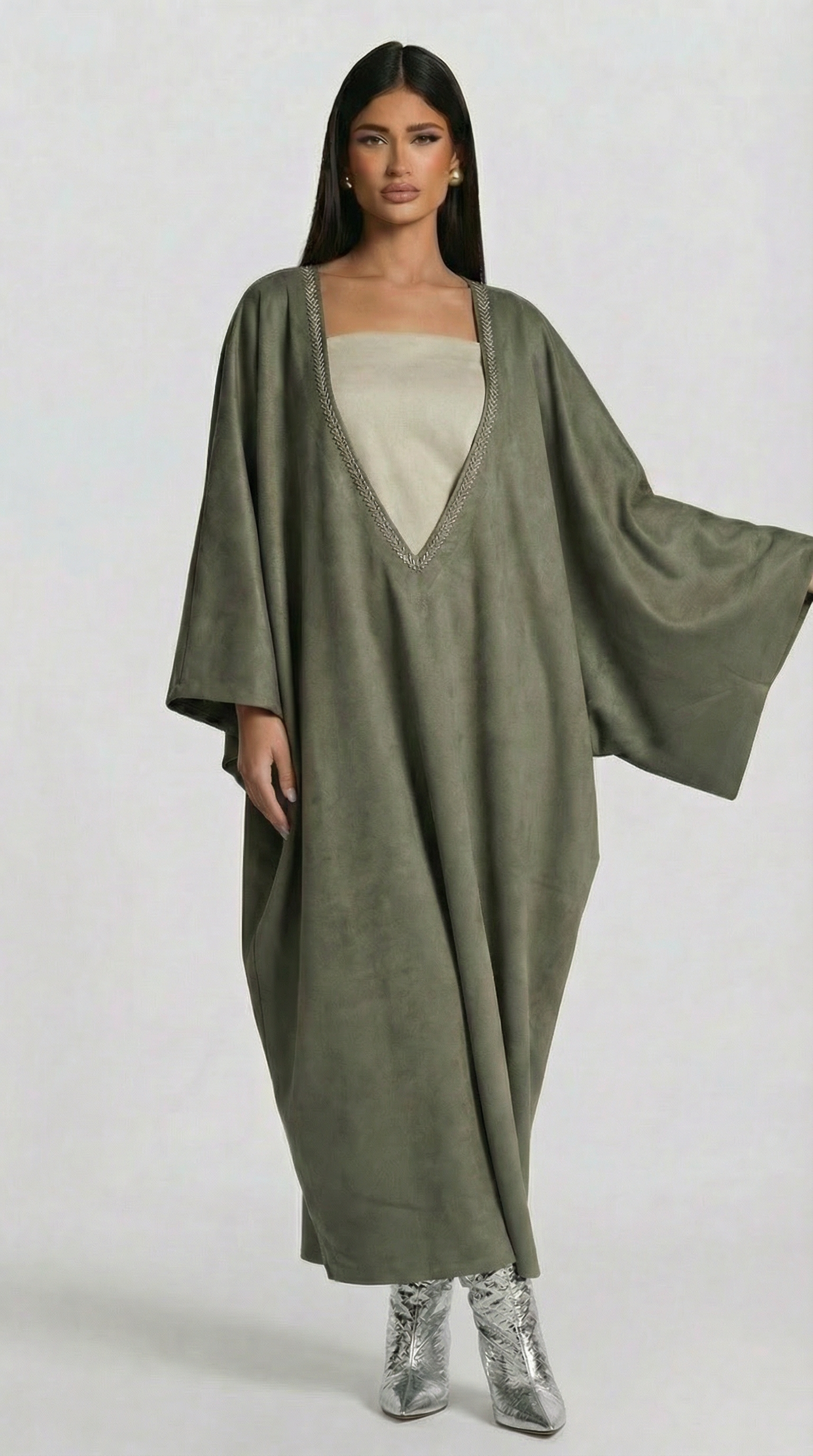 Woman wearing a long olive green dress with a white top on a white background