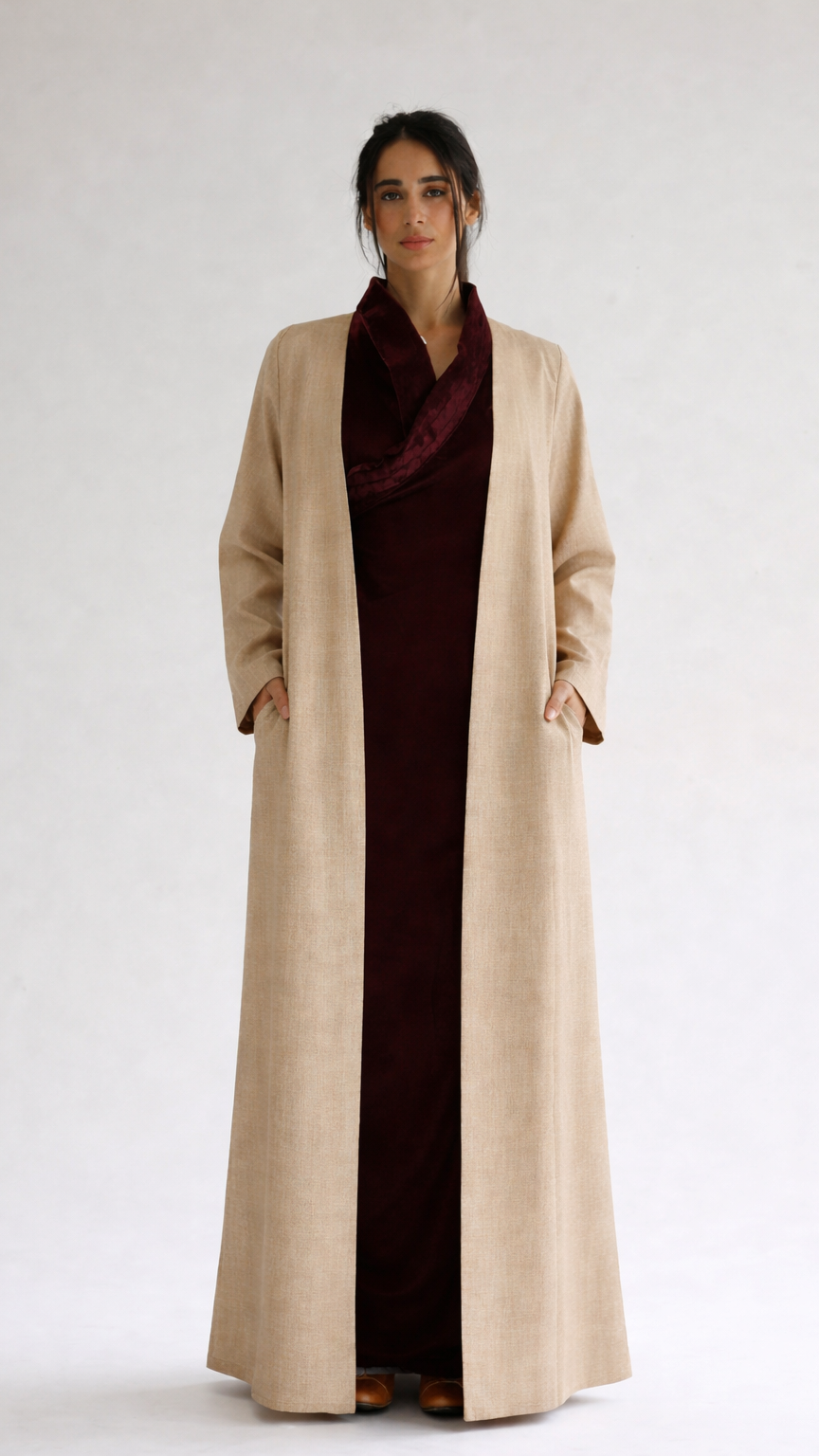 Woman wearing a long beige coat over a dark dress on a white background